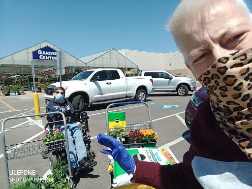 person wearing a cloth face mask standing in the parking lot of a garden center next to shopping carts full of plants