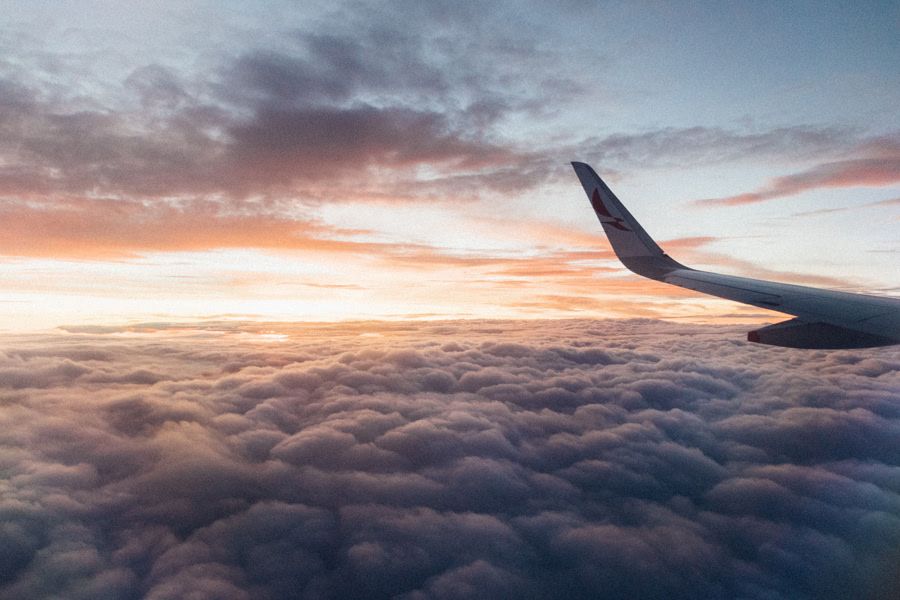 Image of an airplane wing flying over clouds with a sunset in the background